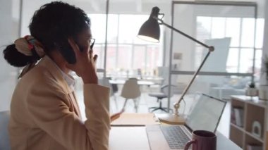 Afrika kökenli güzel Amerikalı iş kadınının tam 360 izleme görüntüsü ofis masasında oturup cep telefonu konuşması sırasında erkek arkadaşı arka planda çalışırken bir şeyi açıklıyor.