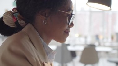 360 derece göğüs hizasında gözlüklü güzel Afro-Amerikalı iş kadınının çalışma saatleri boyunca bilgisayarda çalışırken gülümsemesi ve çalışması.