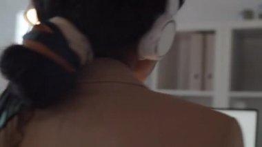 Güzel Afrikalı Amerikalı iş kadınının 360 derecelik görüntüsü. Kafasını ritme göre sallıyor ve ofiste kablosuz kulaklıkla müzik dinlerken şarkı söylüyor.