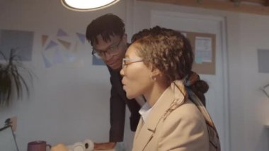 Afrika kökenli Amerikalı erkek ve kadın meslektaşların ofiste birlikte çalışırken dizüstü bilgisayarla projeyi tartışmalarını gösteren bir fotoğraf.