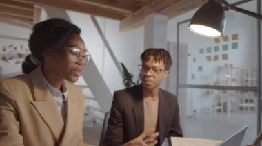 Genç Afrikalı Amerikalı iş adamının 360 derecelik izleme görüntüsü. Kadın meslektaşının yanında oturuyor ve birlikte çalışırken dizüstü bilgisayarında projeyi tartışıyorlar.