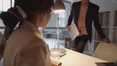 Afrika kökenli Amerikalı kadın yöneticinin 360 derecelik izleme görüntüsü. Masada notlar alıyor, genç bir erkek çalışanla şirket ofisinde çalışırken mali raporları tartışıyor ve kontrol ediyor.