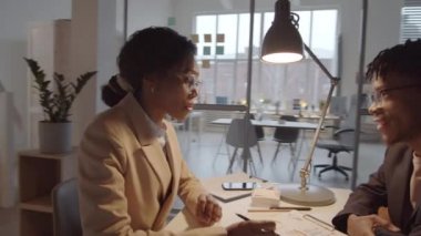 Afrika kökenli Amerikalı bir kadın yöneticinin ofiste birlikte otururken genç bir erkek meslektaşla iş konuşurken tam 360 görüntüsü.