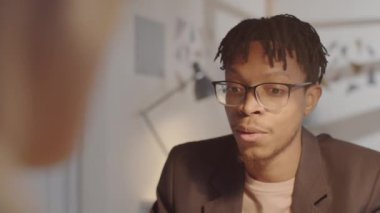 Ofisteki iş görüşmesi sırasında tanınmayan bir yöneticiyle konuşan gözlüklü ve şık giyinmiş Afro-Amerikan genç adamın arkası.