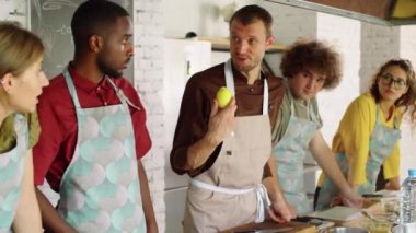 Limon tutan ve yemek pişirme ustası olan genç çoklu etnik gruptaki bir grup insana tarifi açıklayan bir erkek şef.