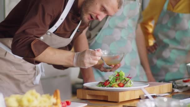 Professioneller Männlicher Koch Schürze Gießt Salatdressing Über Blattsalat Auf Teller — Stockvideo