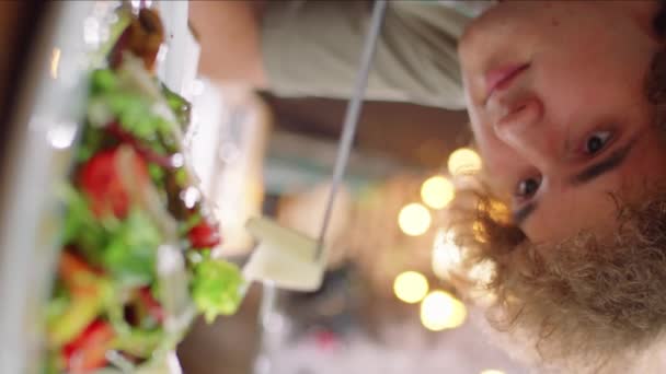 年轻人在用镊子把烤奶酪条放在盘上的沙拉上时的垂直齿条聚焦镜头 — 图库视频影像