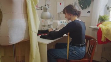 Kadın terzinin dikiş makinesiyle kumaşı dikerken stüdyoda yanan tütsü çubuğuyla çalışırken resmini yakınlaştır.