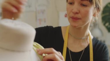 Moda atölyesinde yeni kıyafetler üzerinde çalışırken elbise formundaki güzel terzi kumaşı dikiş iğneleriyle örtünüyor.