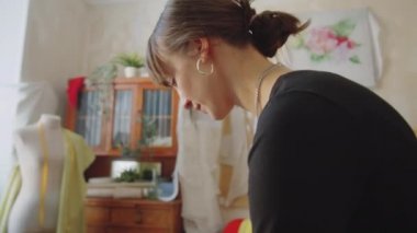 Terzi dükkanında çalışırken dikiş dikmek için kumaş ütüleyen genç ve güzel bir kadın.