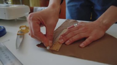 Tanımlanamayan kadın terzinin tebeşir ve cetvelle kumaşa çizdiği elleri yakın çekim.