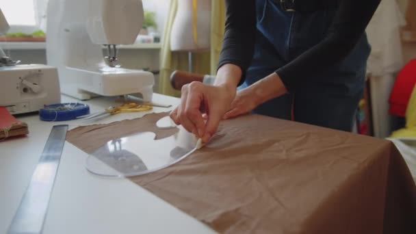 チョークとフランスの曲線定規を使用して若い女性のドレスメーカーは 縫製スタジオで作業テーブルで生地に描画しながら — ストック動画