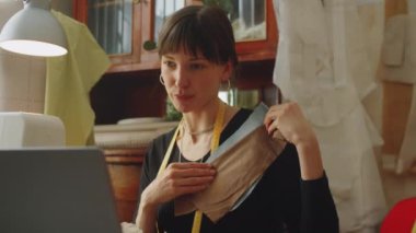 Güzel bayan terzi dikiş atölyesinde oturuyor ve dizüstü bilgisayarla kumaşı tartışıyor.