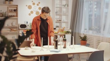 Beyaz bir adam akşam yemeği için sofra kuruyor, güzel karısıyla konuşuyor ve gülüyor.