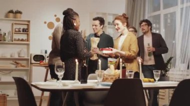 Genç adam ve kadın, Afrikalı Amerikalı arkadaşlarını kucaklıyor ve evde akşam yemeği için toplanırken onlardan hediyeler alıyor.