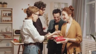 Genç, beyaz bir çift, arkadaşlarına sarılma ve öpücüklerle selam veriyor, hediyelerini açıyor ve evde tatil yemeği için toplanırken şaşırıyorlar.