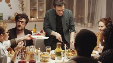 Genç Kafkasyalı adam, arkadaşları için tabağa et koyarken evdeki bayram yemeği sırasında onlara bakıyor.