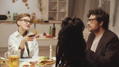 Kafkasyalı bir adam kadeh kaldırıyor, çok ırklı arkadaşlarla kadeh tokuşturuyor ve ev yemeği partisinde şarap içiyor.
