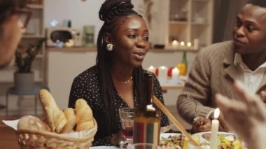 Neşeli bir Afrikalı erkek ve kadın yemek yiyor, arkadaşlarıyla sohbet ediyor ve ev yemeği partisinde gülüyor.