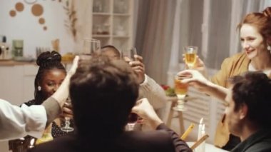 Neşeli çoklu etnik çeşitlilikte kadın ve erkeklerin kadeh tokuşturması, şarap içmesi, konuşması ve ev yemeği partisinde yemeğin tadını çıkarması.