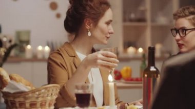 Genç, güzel bir kadın elinde şarap kadehiyle arkadaşlarıyla konuşuyor ve akşam yemeği partisinde gülümseyerek kameraya bakıyor.