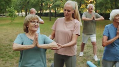 Genç bayan eğitmen, parkta yoga yaparken Namaste 'ı nasıl tutacaklarını öğretiyor.