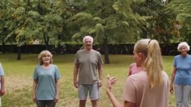 Spor giyimli yaşlı kadın ve erkeklerden oluşan PAN spor salonunda duruyor ve antrenmandan önce genç bayan fitness koçunun talimatlarını dinliyor.