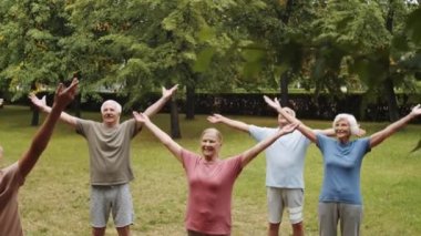 Spor giyim kuşamında spor giyinen yaşlı erkek ve kadınların park yerinde durup, kadın çalıştırıcı ile dışarıda vücut geliştirme kursuna giderken kollarını kaldırışlarını aşağı eğ.