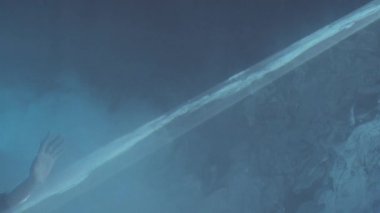 Karanlık stüdyoda sisli sıvı gökyüzü efektiyle düz bir lazer ışığı tabakasında yürüyen genç bir kadının yan görüntüsü