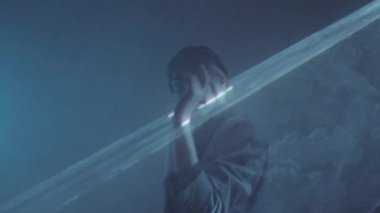 Genç, rahat bir kadın, karanlık stüdyoda sisli ve geniş lazer ışığı projeksiyonuyla dans ediyor.