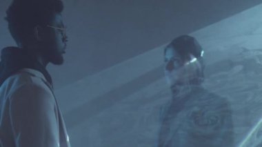 Genç, beyaz bir kadın lazer ışığı tabakasında yürüyor. Sıvı gökyüzü efektiyle ve karanlık odada sevgisi olan Afro-Amerikalı bir adama sarılıyor.