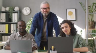 İş dünyasının kıdemli akıl hocası ve genç çoklu etnik kökenli erkek öğrencilerin portresi ofis çalışma gününde kamera önünde birlikte poz veriyorlar.