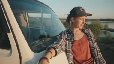 Minibüse yaslanan, kameraya bakıp gülümseyen genç bir kadının görüntüsünü yakınlaştır.