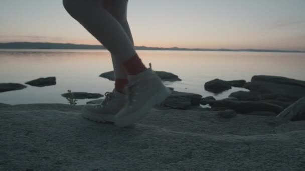 若い女性のゆっくりとした動きのショットを傾ける夏の夜に岩の多い湖畔を歩く — ストック動画