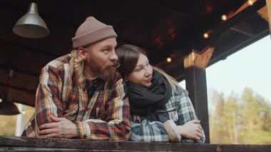 Genç romantik çiftin alçak açılı çekimi. Çiftlik evinin korkuluklarına yaslanmış, başka tarafa bakıyor ve konuşuyor.