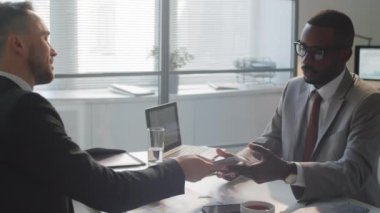 Kafkasyalı iş adamının Afro-Amerikalı erkek meslektaşına sözleşmeyi verirken, ofis toplantısını imzaladıktan sonra onunla konuşup tokalaşırken.