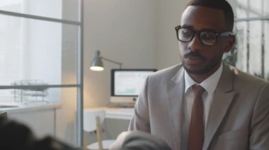 Genç Afro-Amerikalı iş adamının ofis toplantısı sırasında anlaşma imzalaması, konuşması ve Kafkas ortağıyla el sıkışması yüzünden.