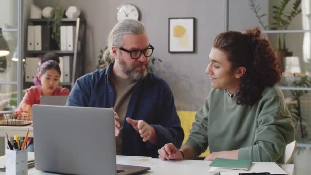 Starszy Męski Mentor Wyjaśniający Projekt Laptopie Młodemu Stażyście Podczas Siedzenia — Wideo stockowe