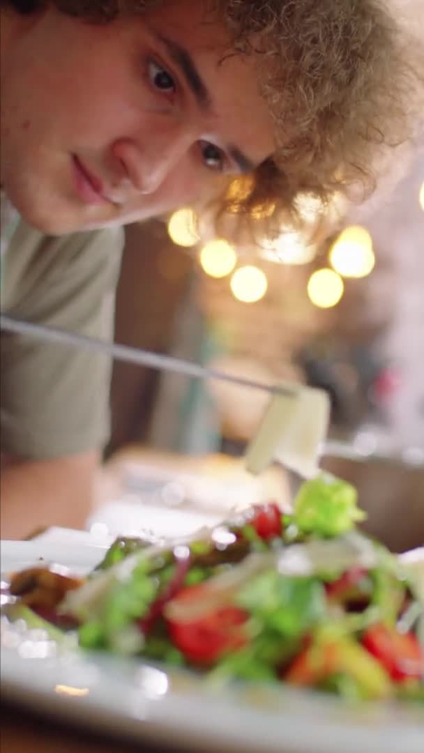 年轻人在用镊子把烤奶酪条放在盘上的沙拉上时的垂直齿条聚焦镜头 — 图库视频影像
