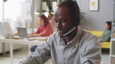 Masada çalışan Afro-Amerikan erkek ajanın portresi. Çağrı merkezinin ofisindeki kameraya bakıyor.