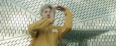 Beyaz tenli genç bir kadın dansçının kameraya bakıp delinmiş duvarın önünde dans edişinin anamorfik pozunu çek.