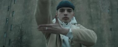 Modayı takip eden ceketli ve şapkalı bir gencin eski beton binanın önünde kameraya bakıp dans ederken anamorfik görüntüsünü yakınlaştır.