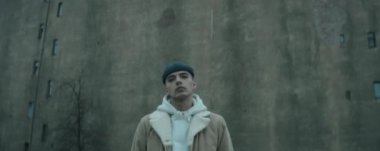 Kendine güvenen modaya uyan ceketli ve şapkalı genç adamın eski beton binanın önünde kameraya bakarken anamorfik görüntüsünü yakınlaştır.