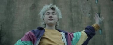 Düşük açılı anamorfik çekim. Klasik ceketli genç bayan dansçı eski beton binanın önünde vogue yapıyor.