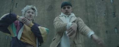 Genç ve şık bir çiftin kameraya bakıp eski beton binaya karşı açık havada vogue dansı yaptığı belden yukarı anamorfik çekim.