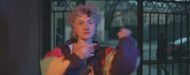 Retro bombardıman ceketi giymiş genç bir kızın avlu kapılarını açtığı, kameraya doğru yürüdüğü ve akşam dans ettiği anamorfik bir sahne.