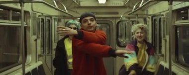 Trendeki iki kızla kameraya bakıp dans eden trend kıyafetli bir gencin anamorfik çekimi.