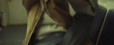 Tramvayda oturan, kameraya bakan ve enerjik kol hareketleri yapan genç ve yakışıklı erkek dansçının anamorfik görüntüsü.