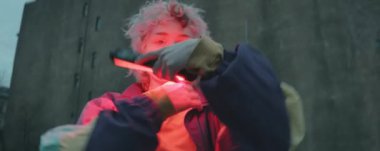 Anamorfik düşük açılı, elinde lamba tutan genç bir kadın, kameraya bakıyor ve sokakta vogue dansı yapıyor.