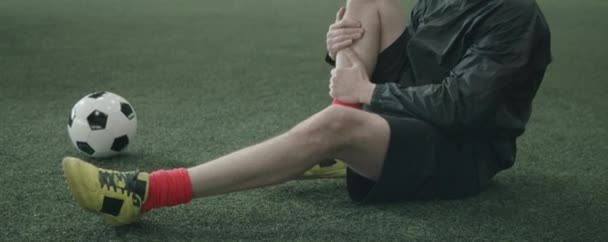 白种人足球运动员穿着运动服坐在室内足球场上 在运动前伸展臀部时双膝压向胸部的变形倾斜镜头 — 图库视频影像
